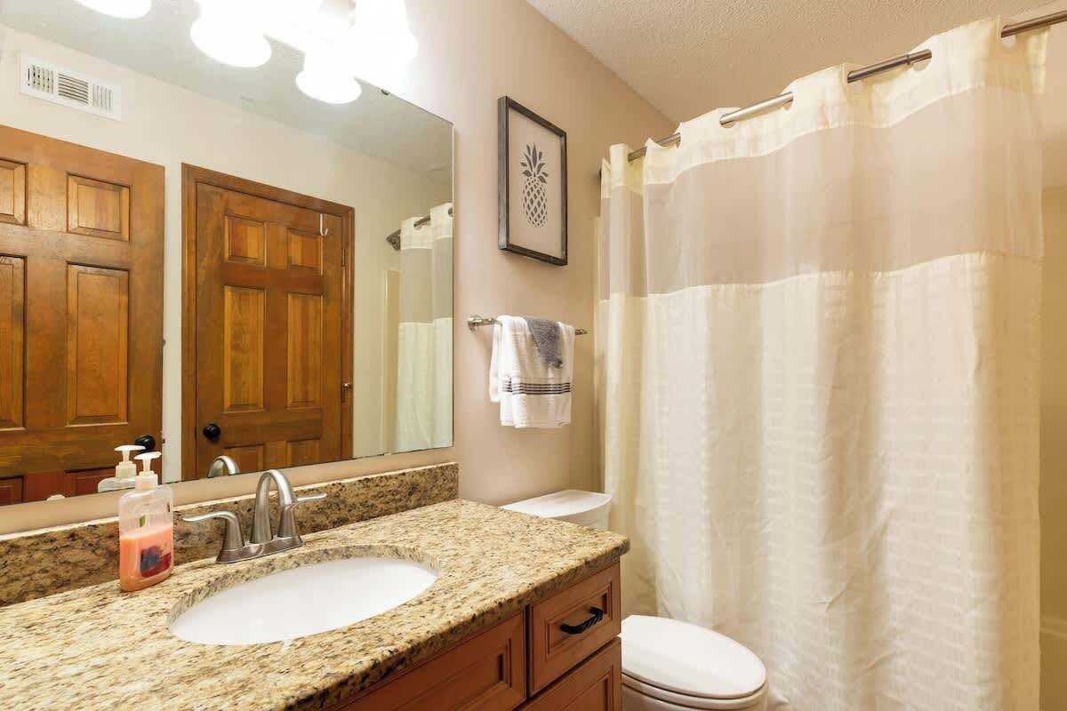A bathroom with a granite sink, a mirror, a toilet, and a shower curtain.