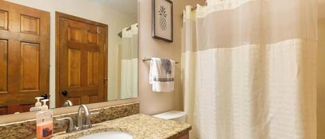 A bathroom with a granite sink, a mirror, a toilet, and a shower curtain.