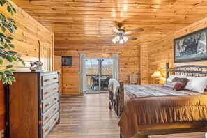 Quarto de cabana de madeira com cama, penteadeira, ventilador de teto e uma janela grande.