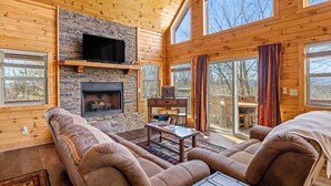 A cozy cabin interior with a stone fireplace, wooden walls, and large windows.