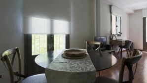A dining area with a round table, chairs, a television, and a desk with a lamp.