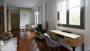 A spacious room with a wooden desk, a chair, a television, and a window with a view of trees.
