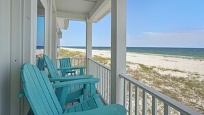 Blick auf einen Strand von einer Veranda aus, mit türkisfarbenen Adirondack-Stühlen.