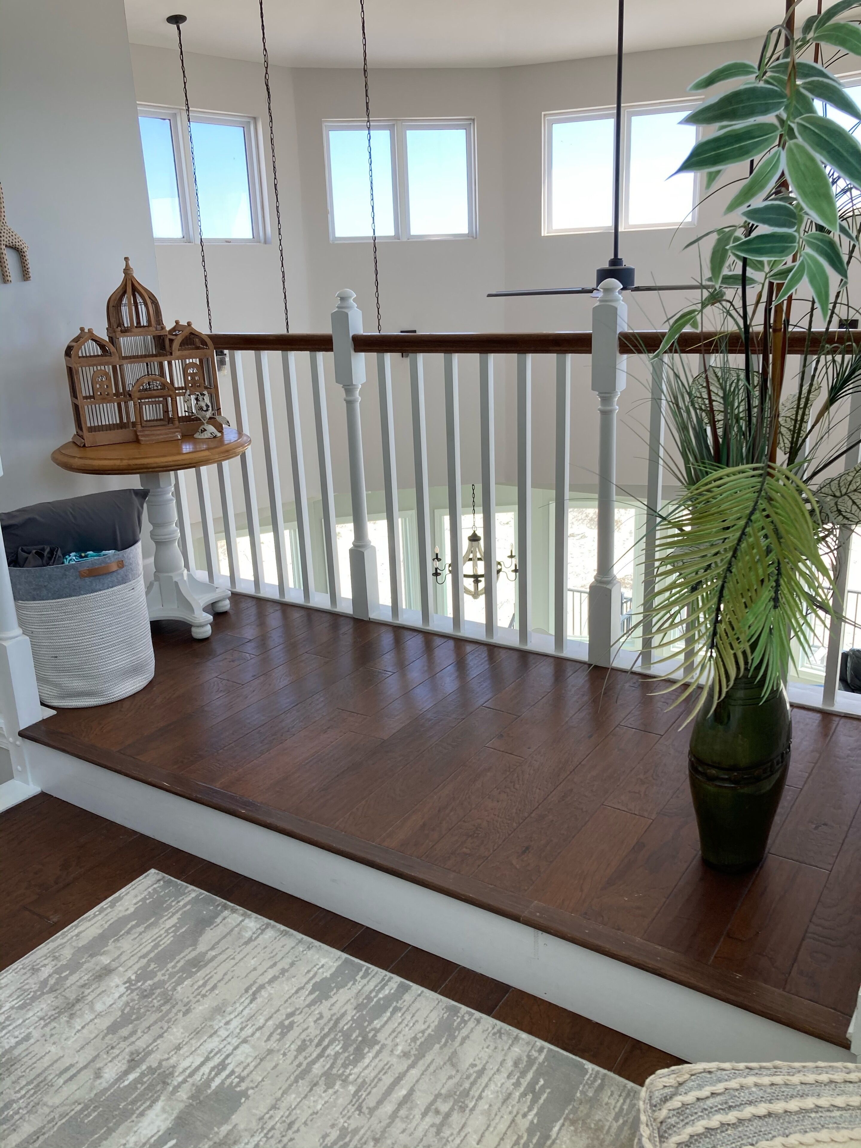 A spacious balcony with a wooden floor, white railing, and a hanging birdcage.