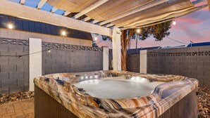 An outdoor hot tub with a marble-like texture, surrounded by a wooden deck and a brick wall.