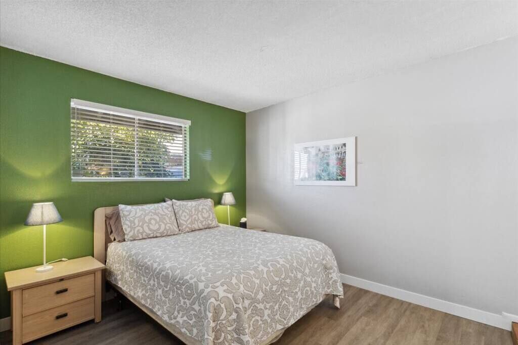 A bedroom with a bed, nightstands, a window, and a framed picture on the wall.