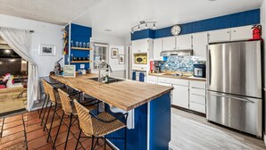 A modern kitchen with a central island, bar stools, a stainless steel refrigerator, and a blue accent wall.