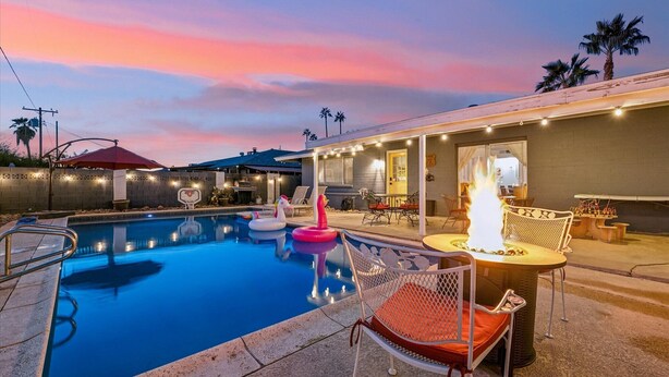 A swimming pool with lounge chairs and a fire feature, surrounded by a covered patio area with tables and chairs.