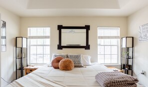 Cozy retreat with a large bed, two windows, and a dark-framed mirror.