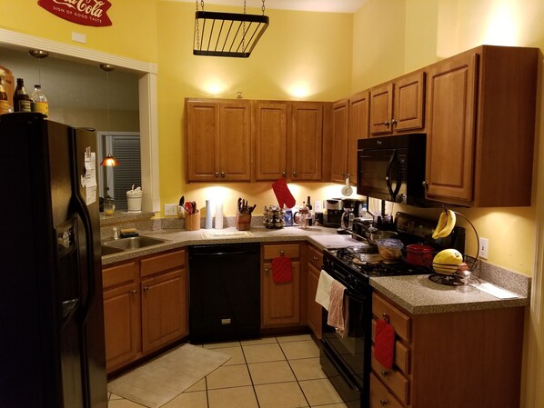 Fully equipped kitchen with refrigerator, stove, and microwave, plus ample storage and a window with blinds.
