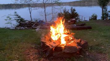 Un feu de camp dans un cadre naturel, avec un lac et des arbres en arrière-plan.