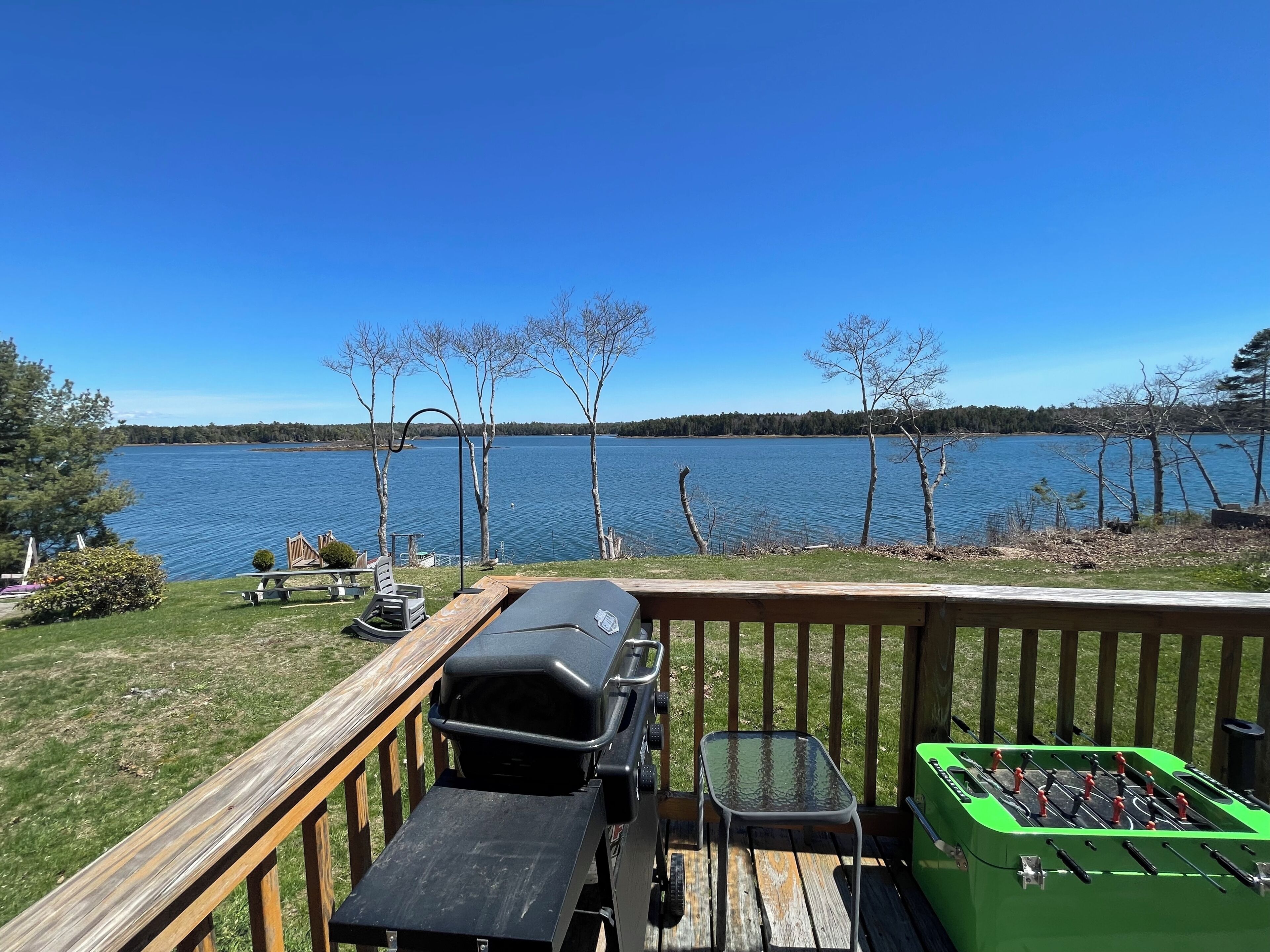 A deck with a grill, a table, and a foosball table overlooking a lake.