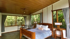 Une chambre spacieuse avec un grand lit, un plafond en bois, un sol en pierre et de grandes fenêtres avec des rideaux.