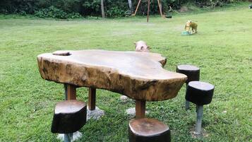 Situated on a well-maintained lawn, this table offers a serene outdoor space surrounded by trees and a nearby swing set.