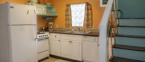 Una cocina con electrodomésticos blancos, encimera de madera y ventana con cortinas.