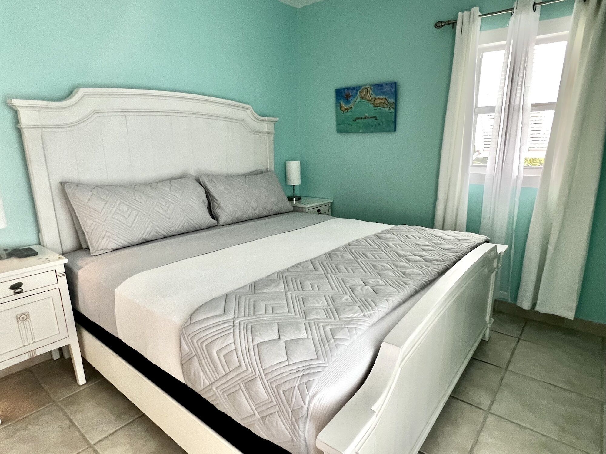 A bedroom with a bed, nightstand, and a painting on the wall.