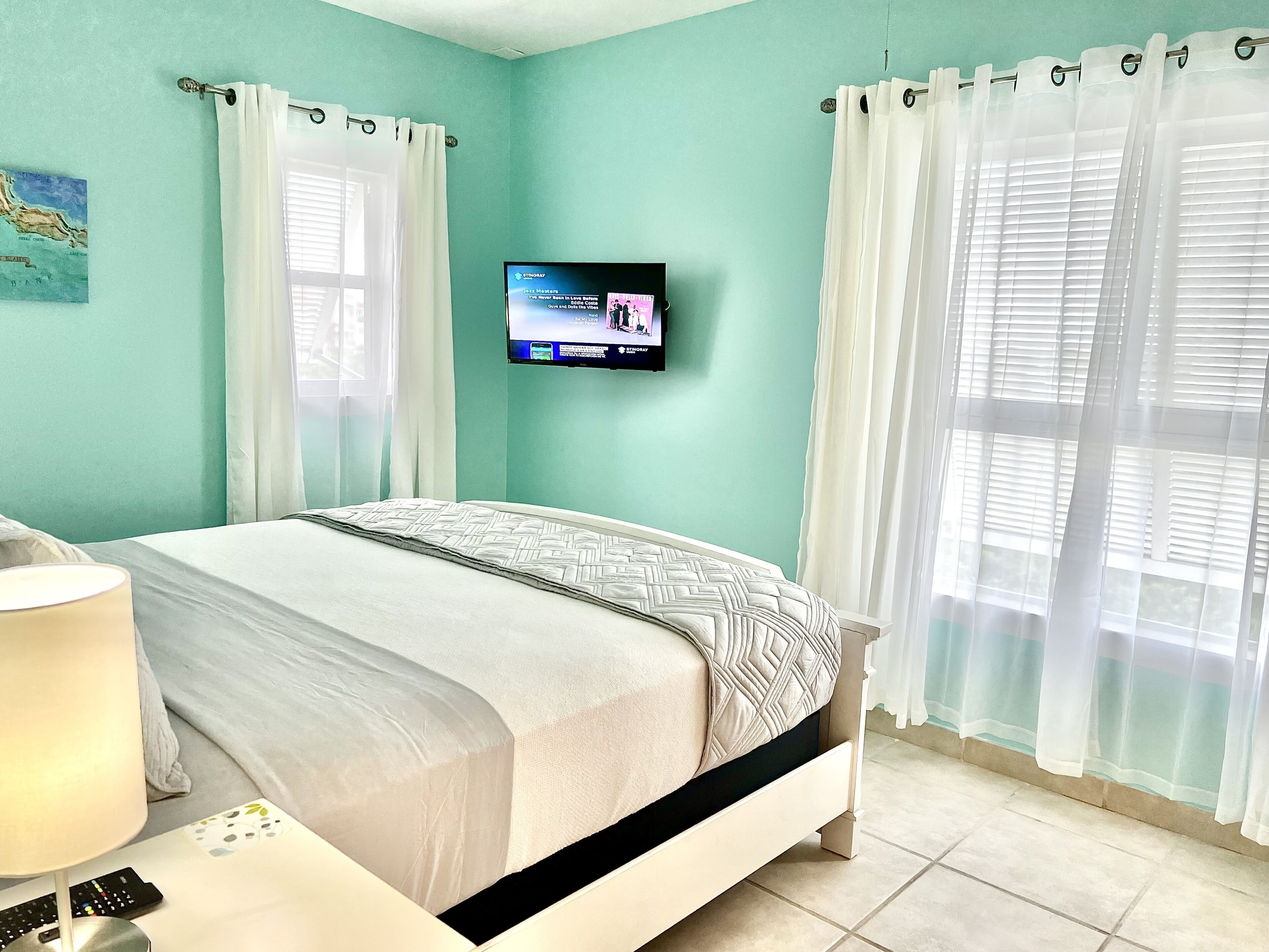 Une chambre à coucher avec un lit, un téléviseur fixé au mur et une fenêtre avec des rideaux.