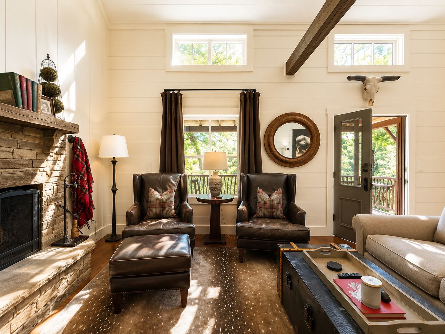 A cozy living room with leather armchairs, a fireplace, a round mirror, and a view of the outdoors.