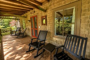 Une véranda en bois avec des fauteuils à bascule, une porte rouge et une pancarte « Bienvenue ».