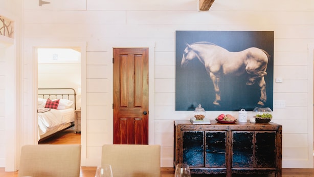 A room with a bed, a dining table with chairs, a wooden cabinet, and a large horse painting on the wall. - Walk to DT Highlands | Designer Cabin | Fireplace | Fenced Yard | Dog Friendly (Highlands)