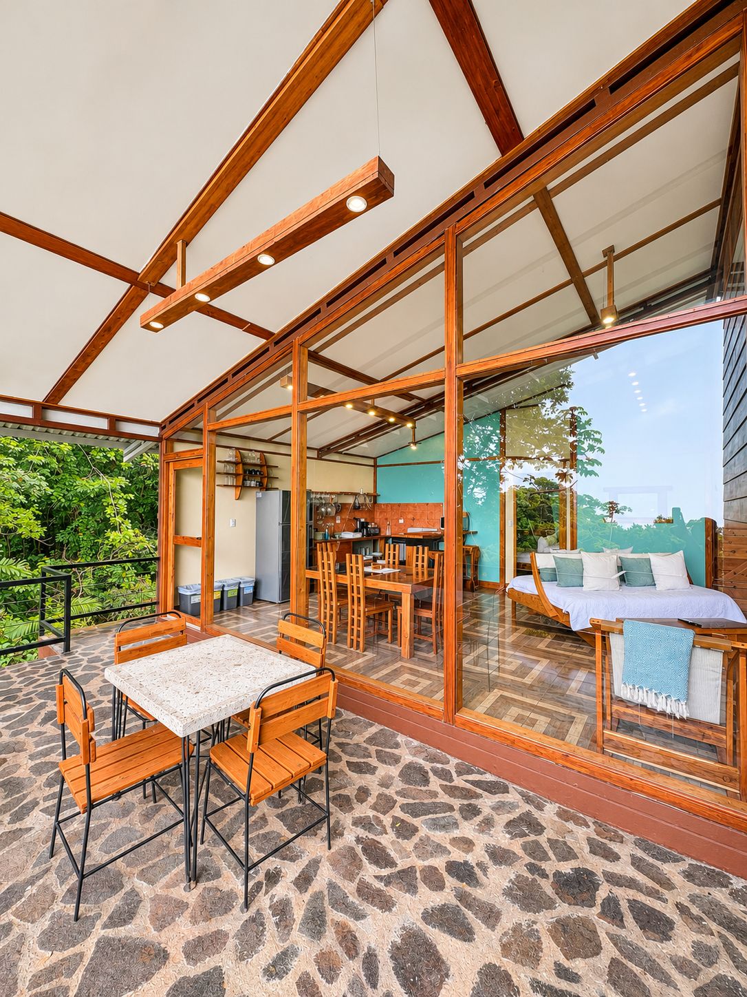 Un amplio espacio al aire libre con mesa y sillas, una zona de cocina y un área de descanso con vistas a la vegetación.