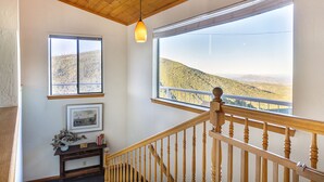 A staircase with wooden balusters leading to a balcony with a view of a hilly landscape.