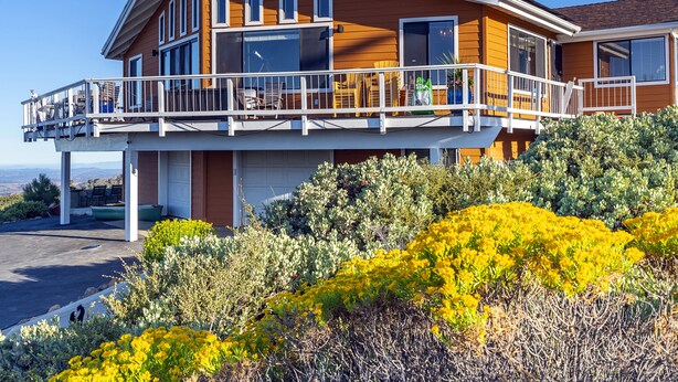 A two-story house with a balcony, a garage, and a view of the landscape.
