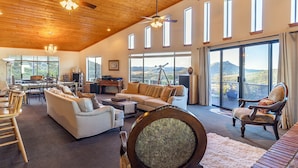 A spacious living area with a high ceiling, large windows, and a balcony with a mountain view.