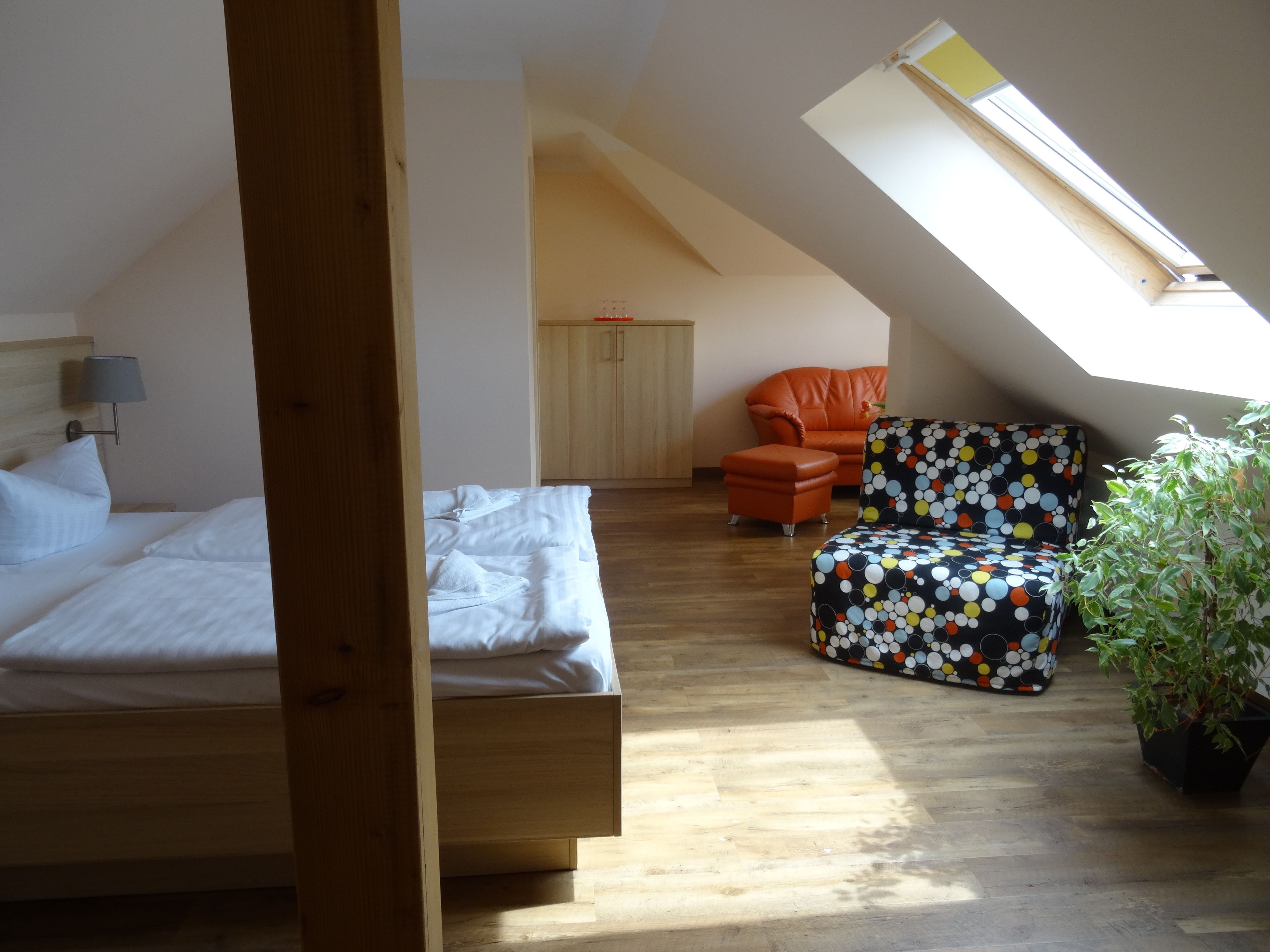 A bedroom with a wooden bed, a small orange chair, a colorful patterned chair, and a skylight.