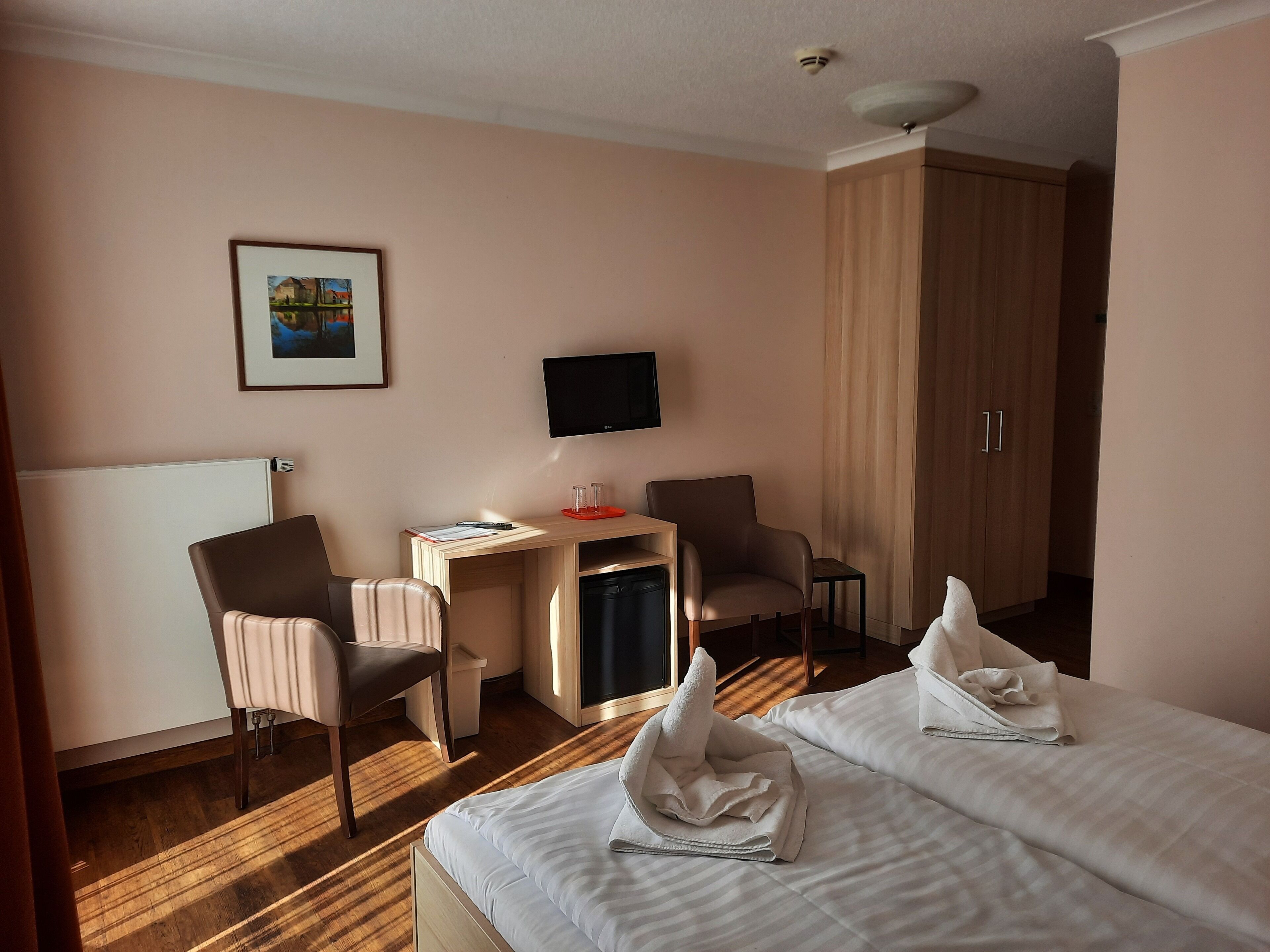 A hotel room with a bed, two chairs, a desk with a computer, a television, and a wardrobe.