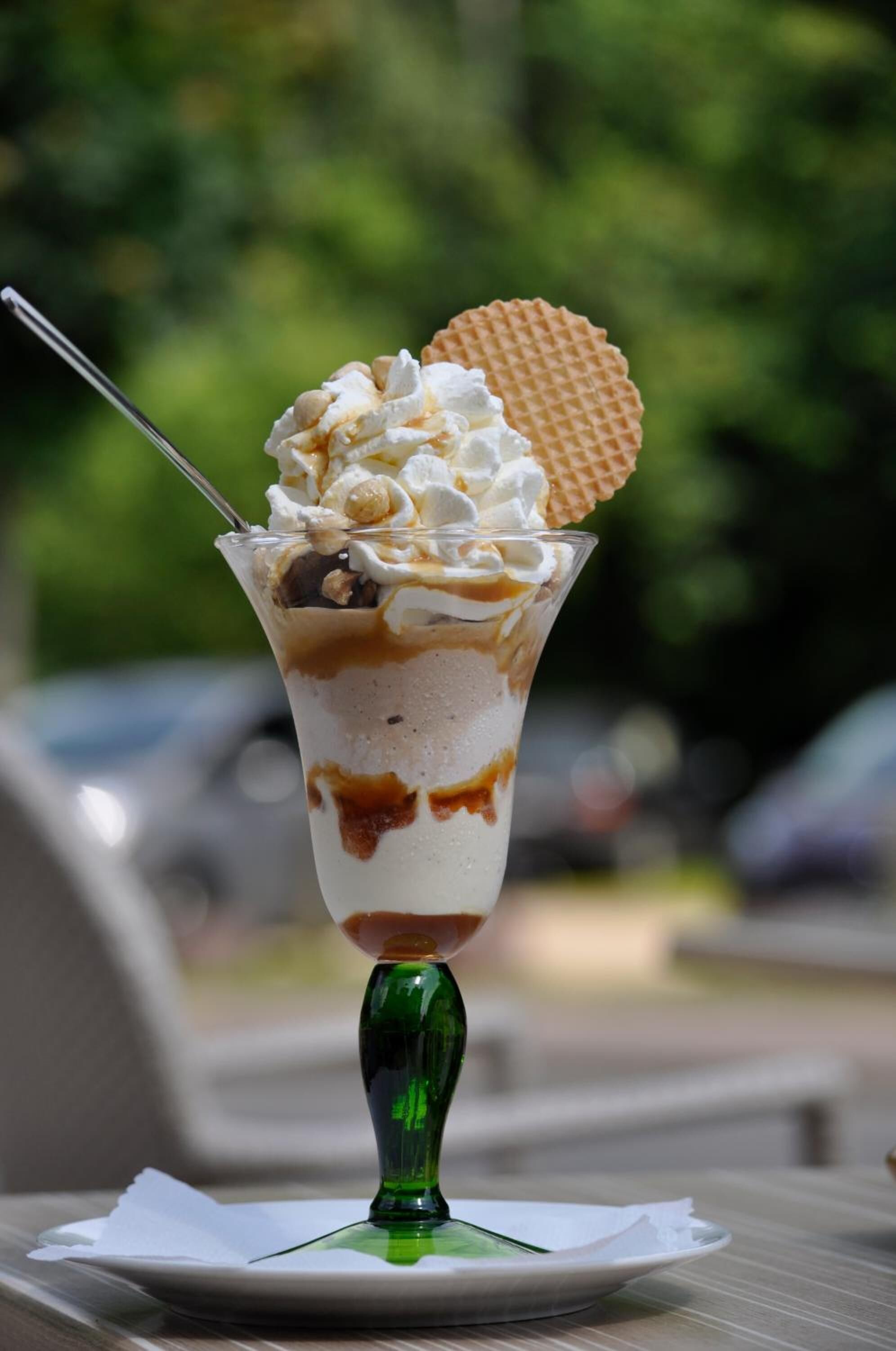 A dessert in a clear glass cup with a waffle on top, placed on a white plate with a green stemmed glass.