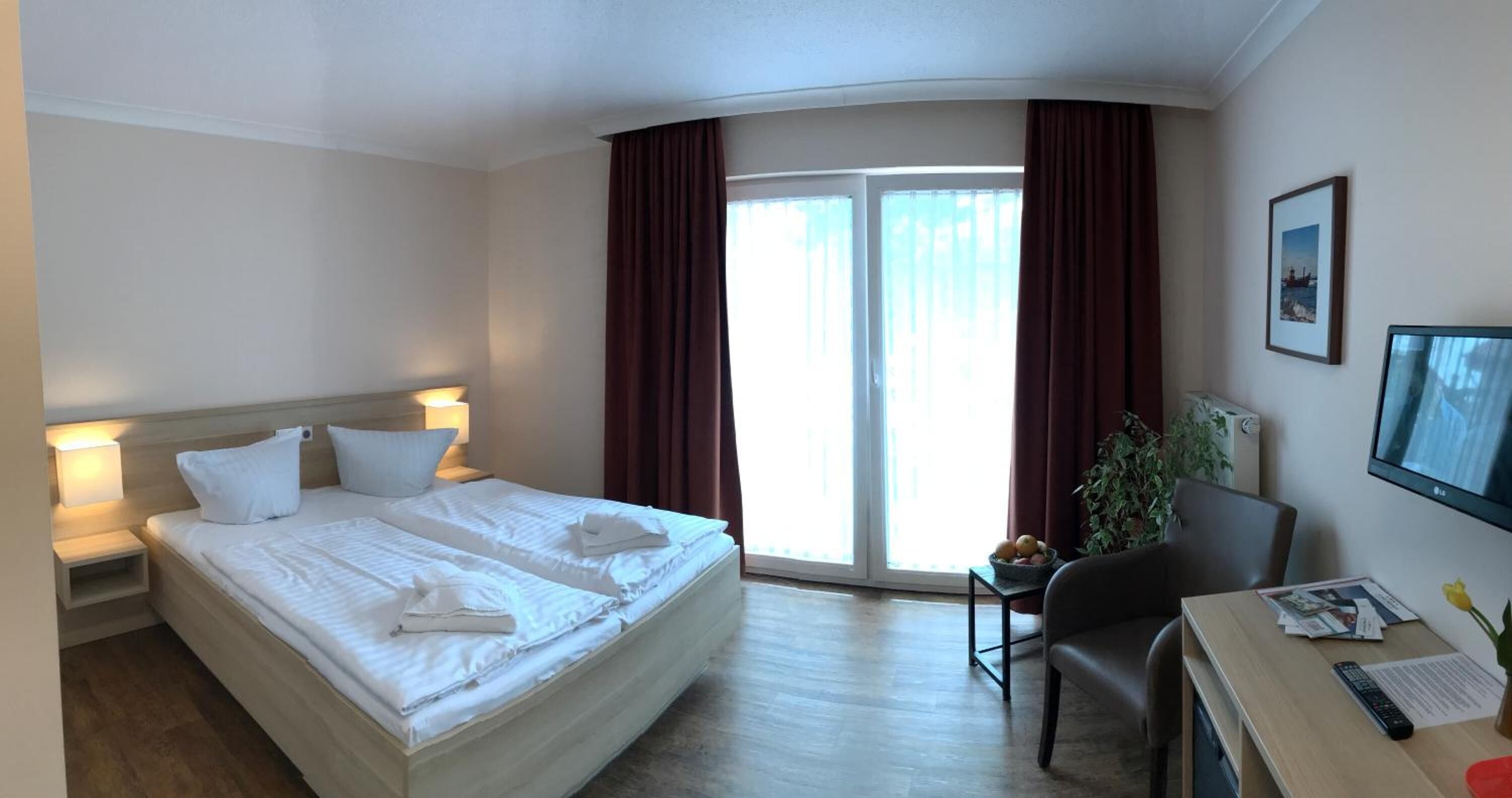 Une chambre d’hôtel avec un grand lit, un bureau avec une chaise, une petite table avec une plante et un téléviseur fixé au mur.