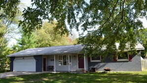 Une maison de plain-pied avec un garage, une véranda et un petit jardin devant.