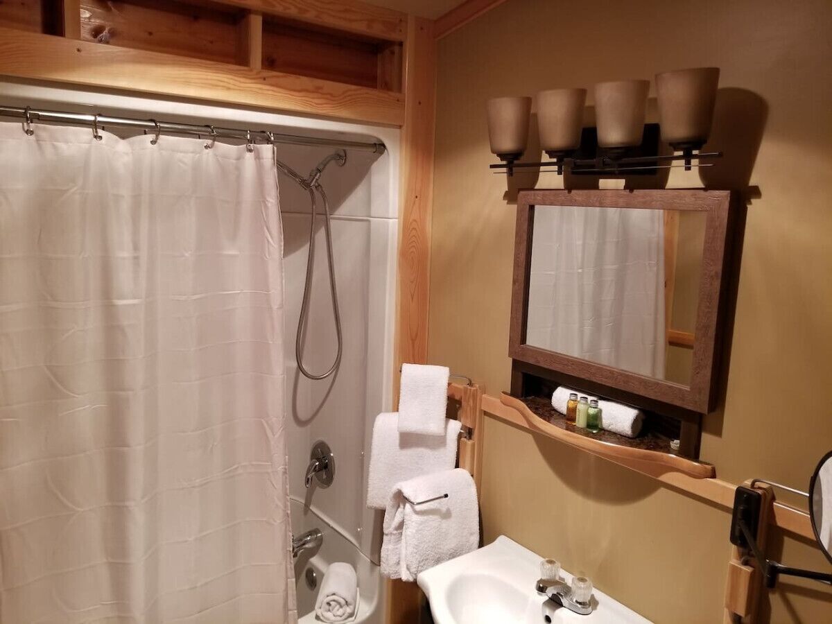 A bathroom with a shower, a sink, a mirror, and a shelf with toiletries.
