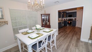 Uma área de refeições com uma mesa branca posta para quatro pessoas, um candelabro e vista para a cozinha.