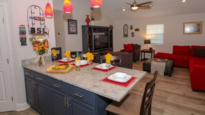 Cozinha moderna com ilha central, área de jantar com jogos americanos vermelhos e sala de estar com sofá vermelho.