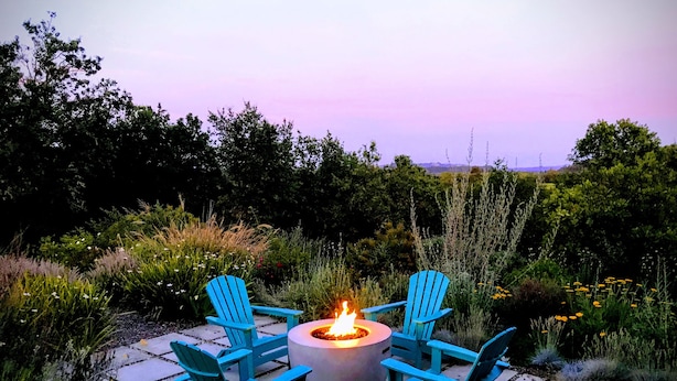 Ein Feuerkorb mit vier blauen Adirondack-Stühlen, die darum angeordnet sind, auf einer Steinterrasse.