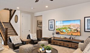 A modern living room with a staircase, a large flat-screen TV, and a comfortable seating area.