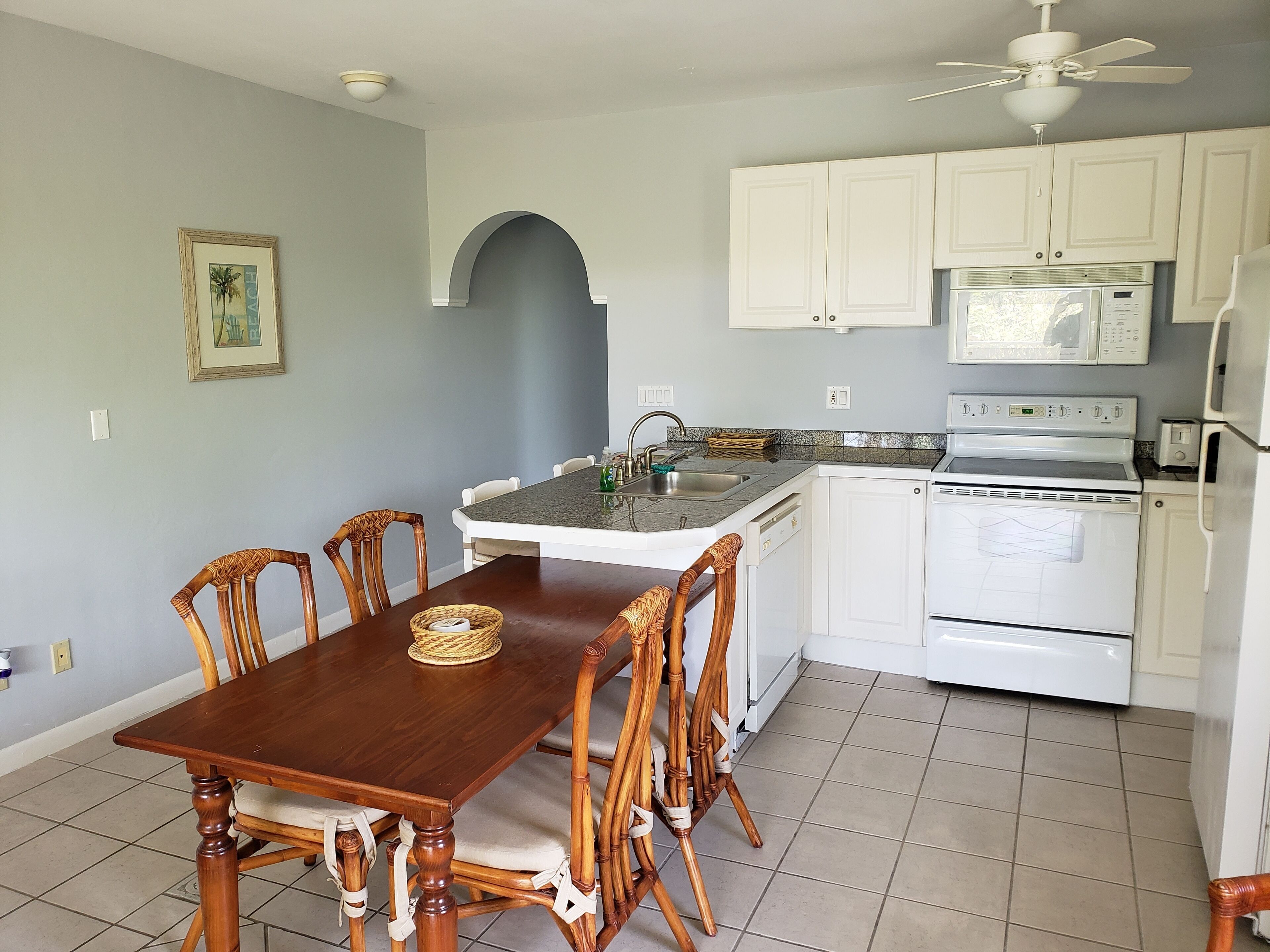 Cocina con armarios blancos, un microondas y un horno. Hay una mesa de comedor con sillas y un cuadro en la pared.