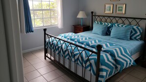Un dormitorio con cama, mesita de noche, ventana con cortinas y aire acondicionado instalado en la pared.