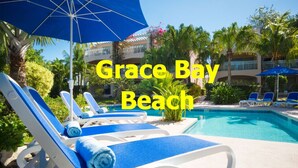 Zona de piscina con sillas de descanso y sombrillas en Playa Grace Bay.