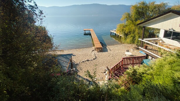 A lakeside property with a wooden dock extending into the water, a small shed, and a building with outdoor seating.