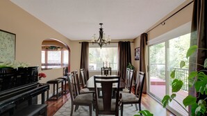 A dining area with a piano, chairs, a chandelier, and large windows with curtains.