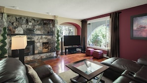 A living room with a stone fireplace, leather sofas, a glass coffee table, and a television.