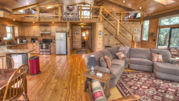 Una cabaña espaciosa con una amplia sala de estar, una cocina y un comedor. Hay una escalera que conecta los dos niveles.