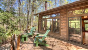 Una cabaña de madera con terraza, ventanas grandes y chimenea.