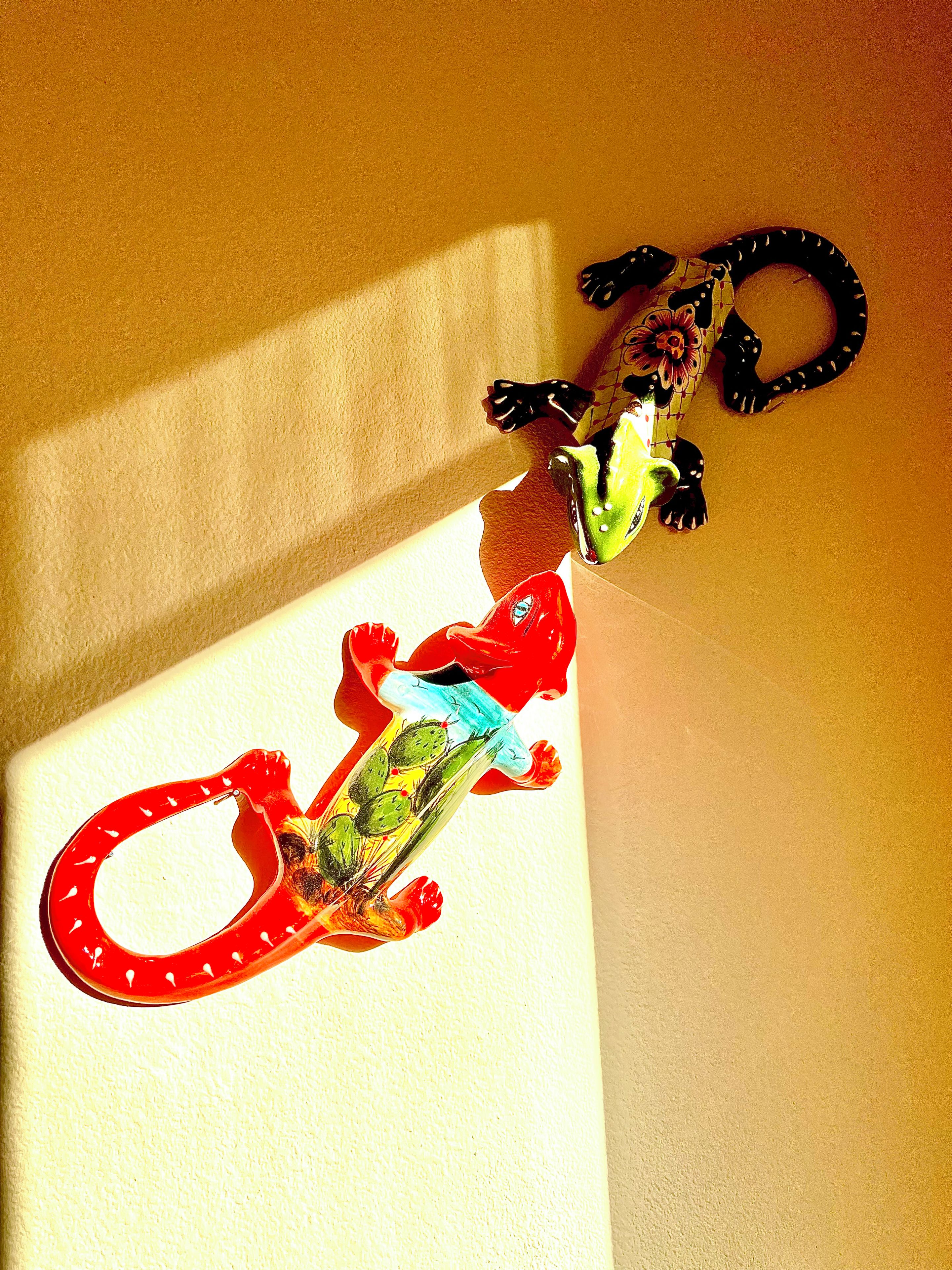 Drei bunte Echsenfiguren an einer Wand.