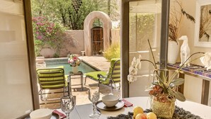 Zona pranzo con vista su una piscina, sedie da esterno e un tavolo apparecchiato con piatti, ciotole e un bicchiere.