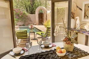Comedor con vista a una piscina, sillas exteriores y una mesa dispuesta con platos, recipientes y un vaso.