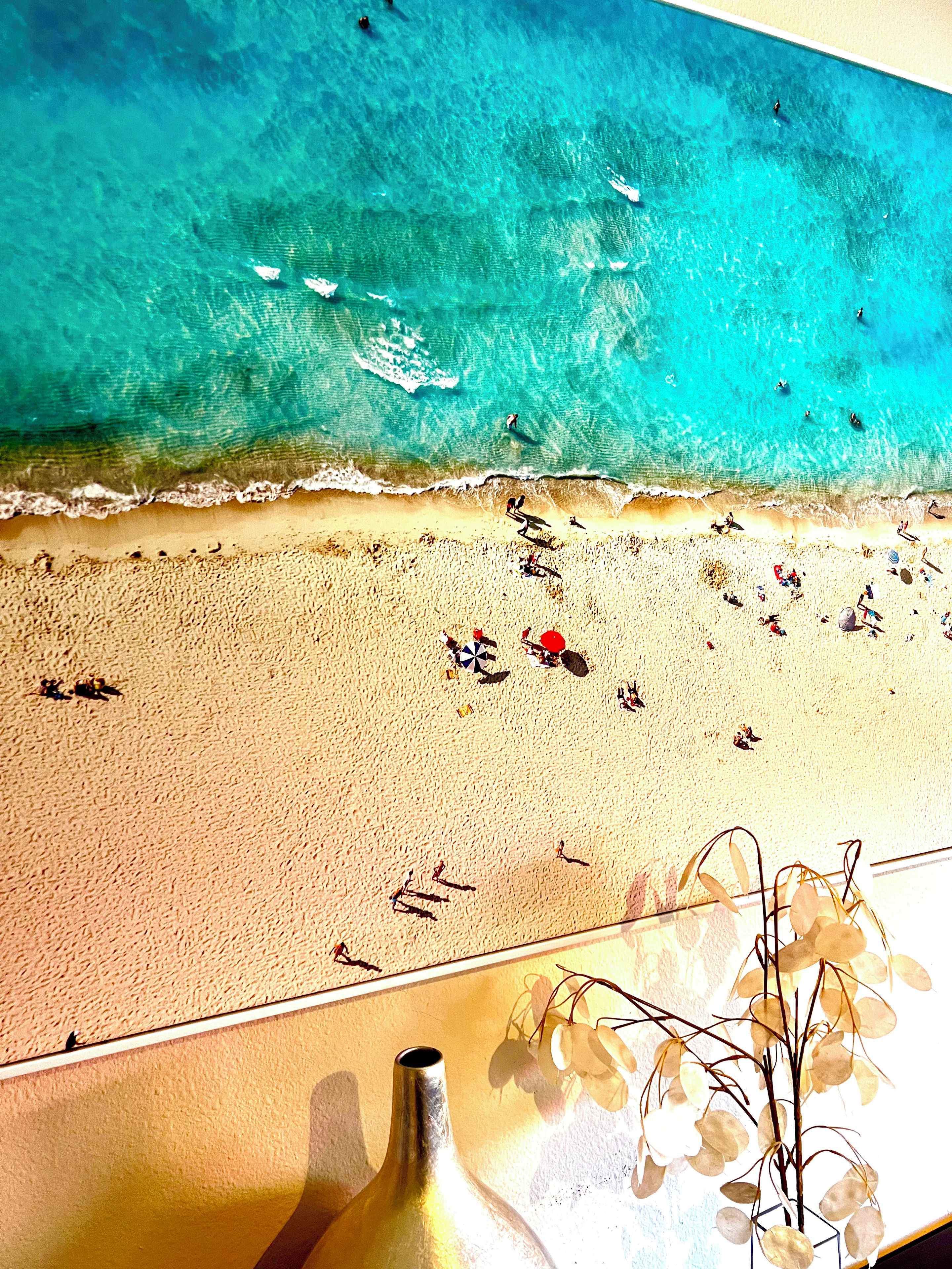 Une scène de plage avec une eau turquoise et limpide, un rivage sablonneux et un vase décoratif rempli de fleurs.